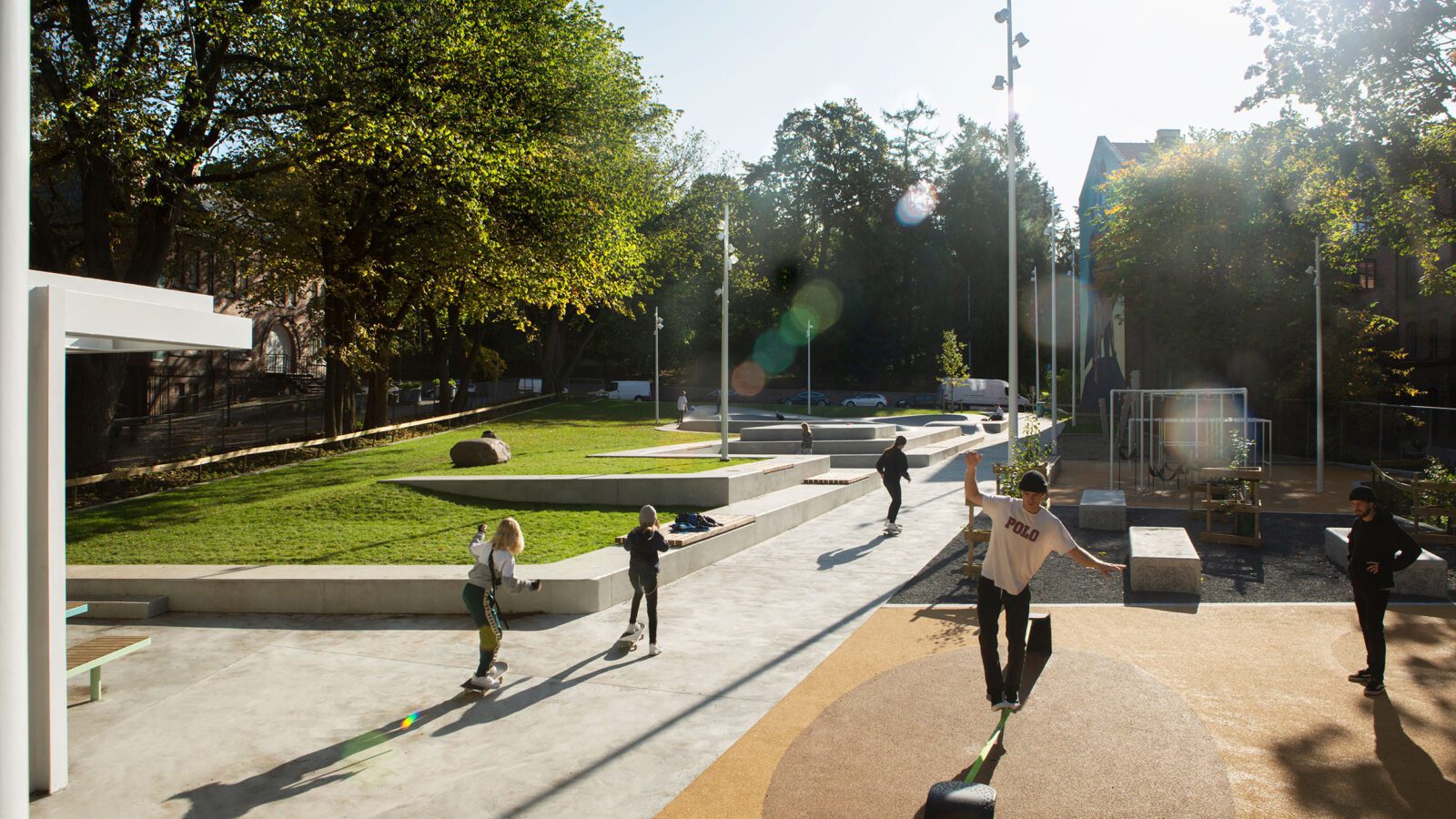 En park med trær. lekeplass og skatepark hvor det er noen barn på skateboard.
