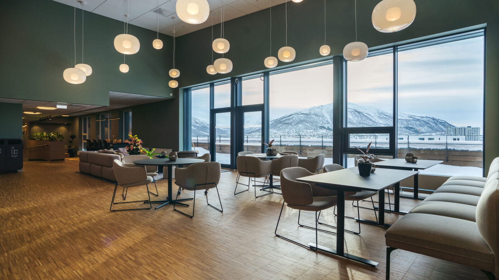 Sittegrupper inne i et næringsbygg med store vinduer og utsikt mot fjellene.