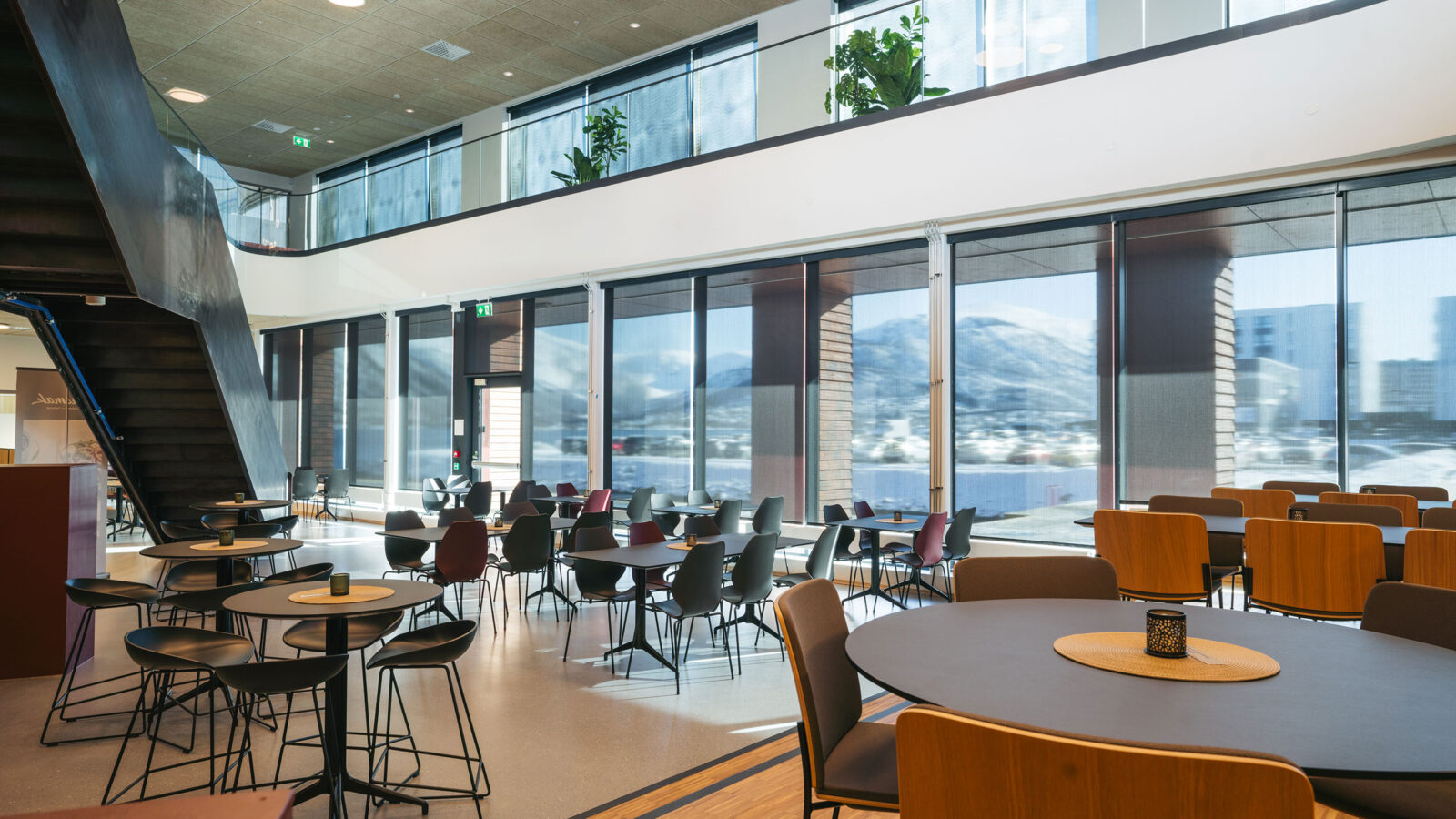 Innsiden i et næringsbygg med store vinduer ut mot sjøen og stoler og bord inne.