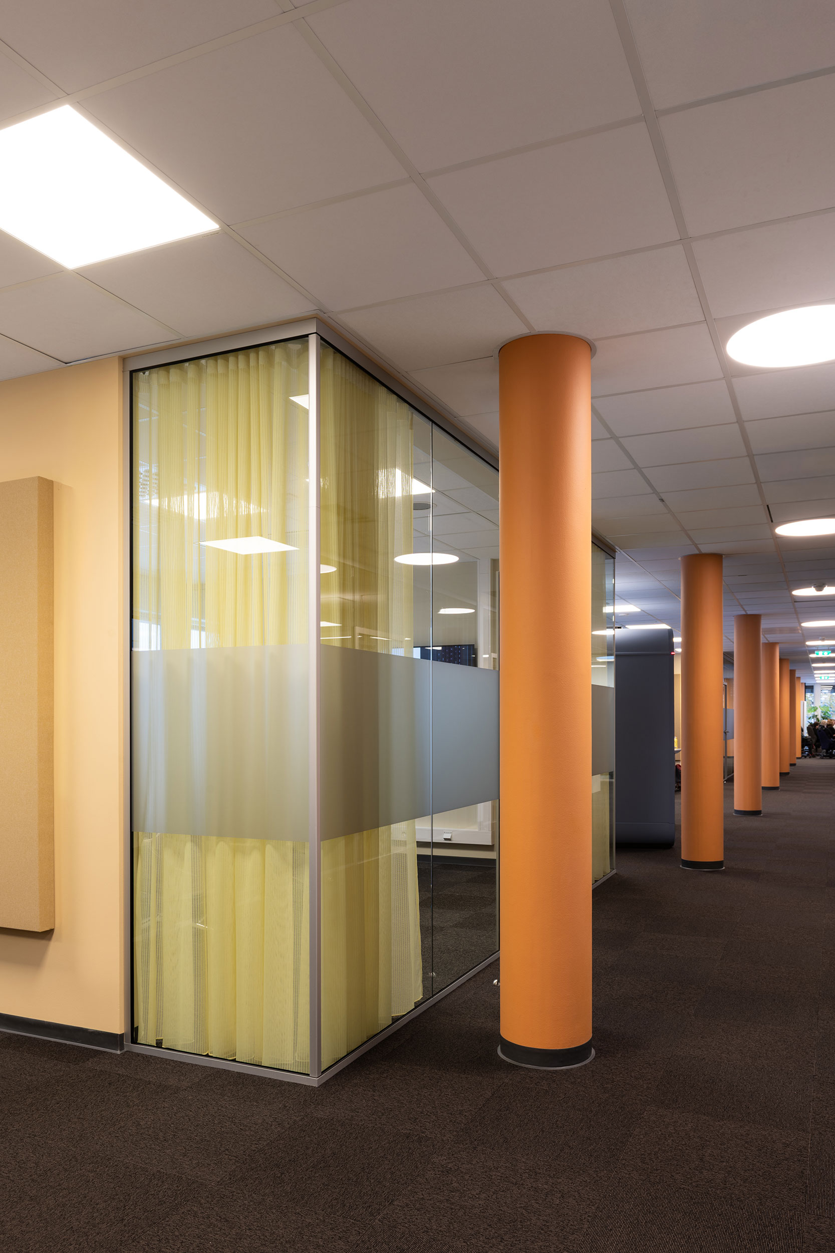 Interiørbilde av NRK Tromsø som viser møterom fra utsiden og en gang med oransje søyler.