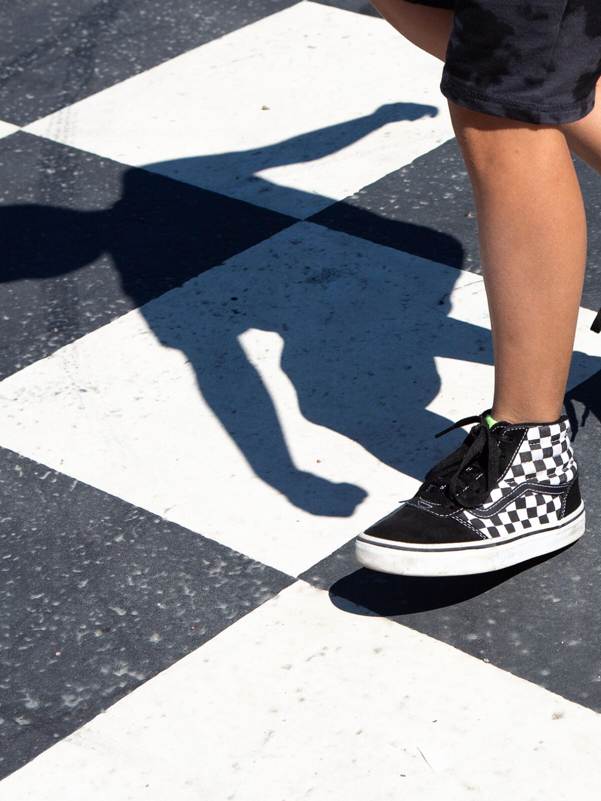 malt sjakkbrett på asfalt og bena til et barn som løper over.