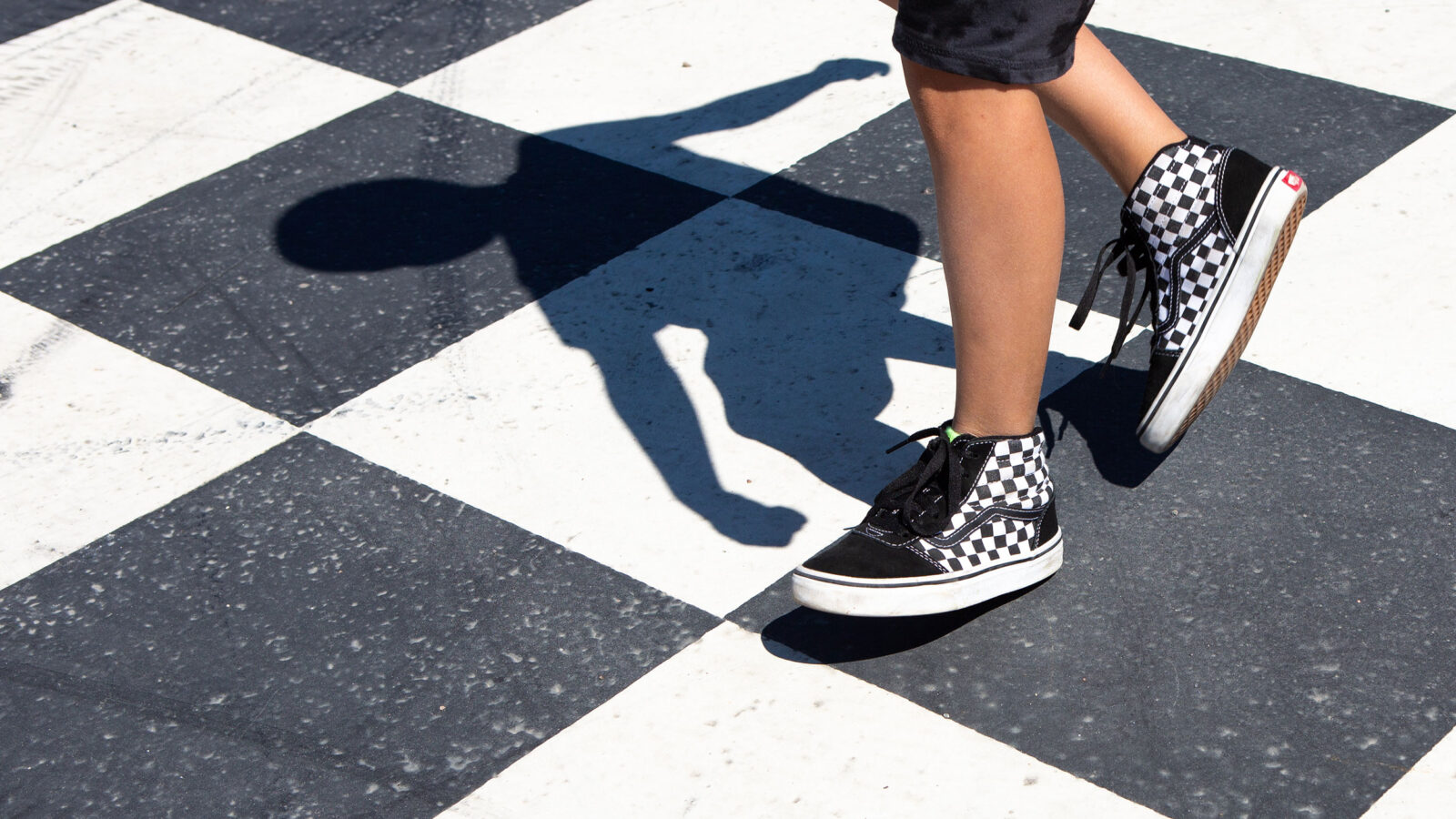 malt sjakkbrett på asfalt og bena til et barn som løper over.