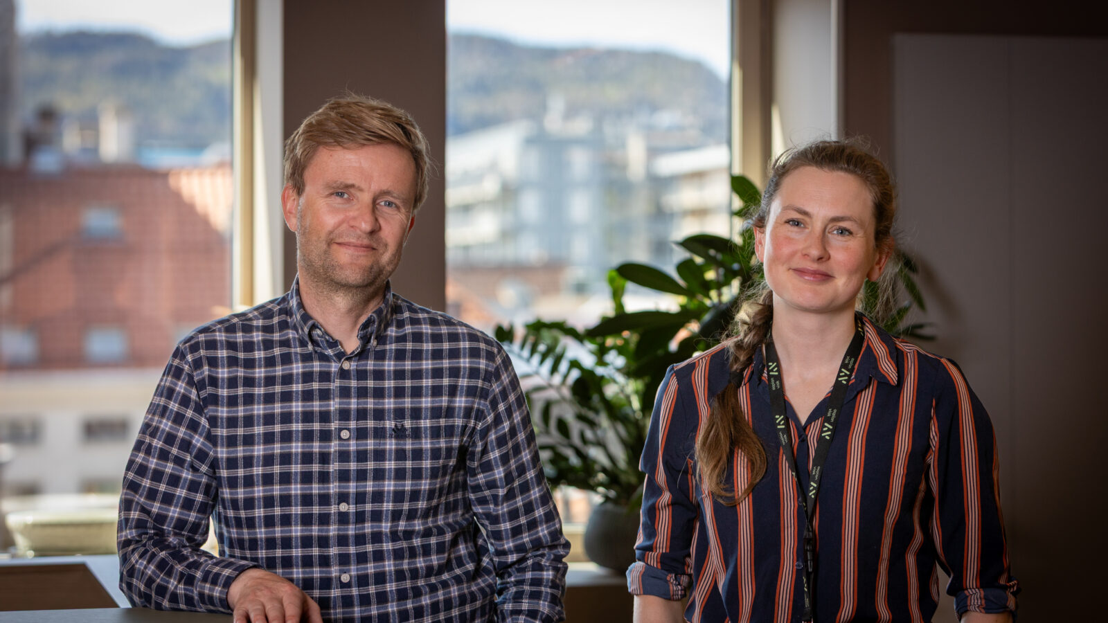 Mannlig og kvinnelig rådgiver foran et vindu med byen i bakgrunnen.