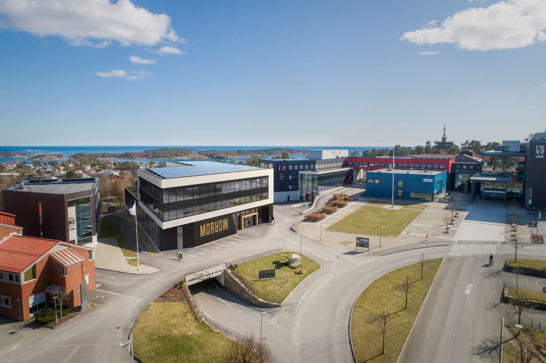 Oversiktsbilde av Morrow Battery Innovation Centre (BIC) på Campus Grimstad, med moderne bygg, campusområde og sjøen i bakgrunnen.