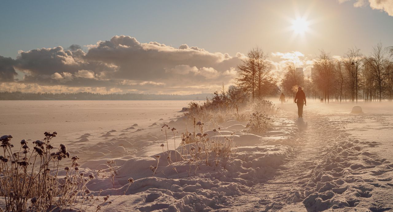 Person går tur langs kysten i snø, frostdis og blek vintersol.