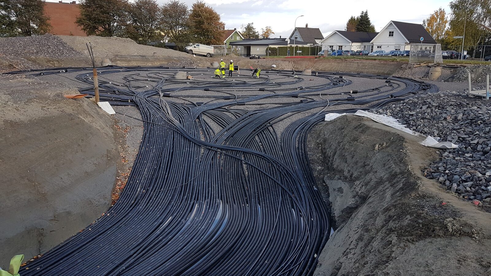 A bundle of thick black cables forms a loop on the ground in an area the size of a football pitch. People wearing high-visibility clothing are working on the installation.