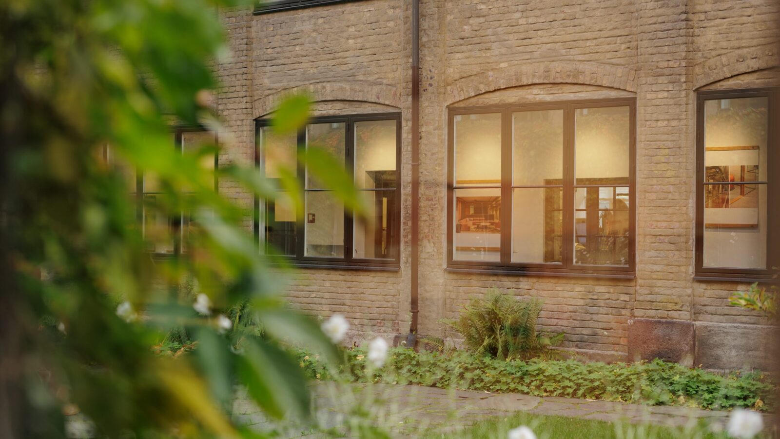 An atmospheric view of green courtyard surrounded by brick buildings, with offices visible through the windows.