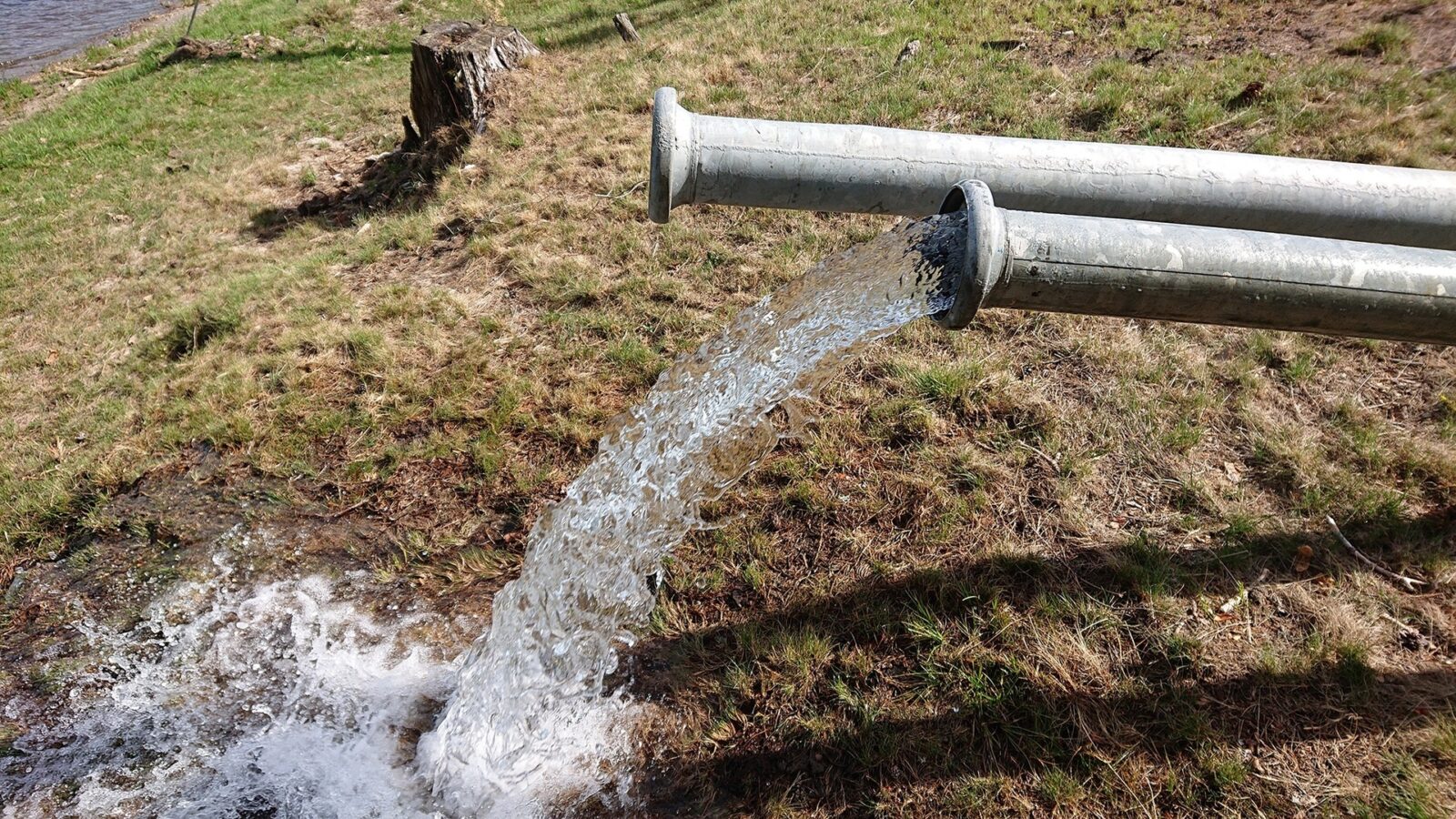 Two well pipes protrude from the ground, with clean water gushing from one of them.