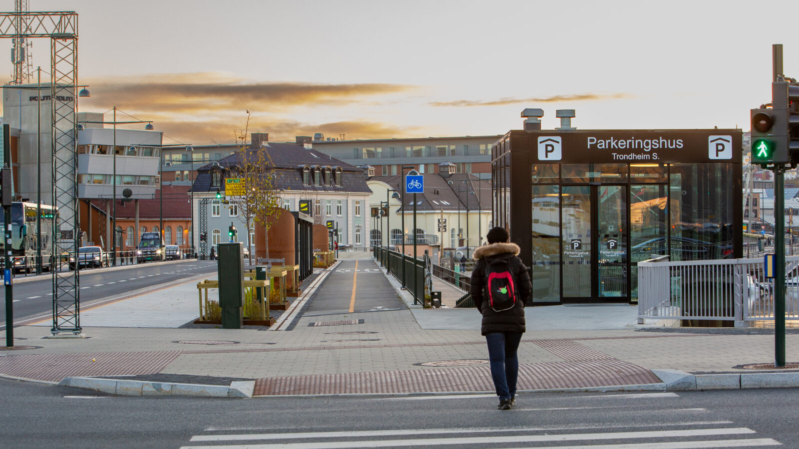 Rear view of a person crossing a street at an accessiblity-marked pedestrian crossing. In the background are a shared cycle and pedestrian path and the entrance to an underground car park.
